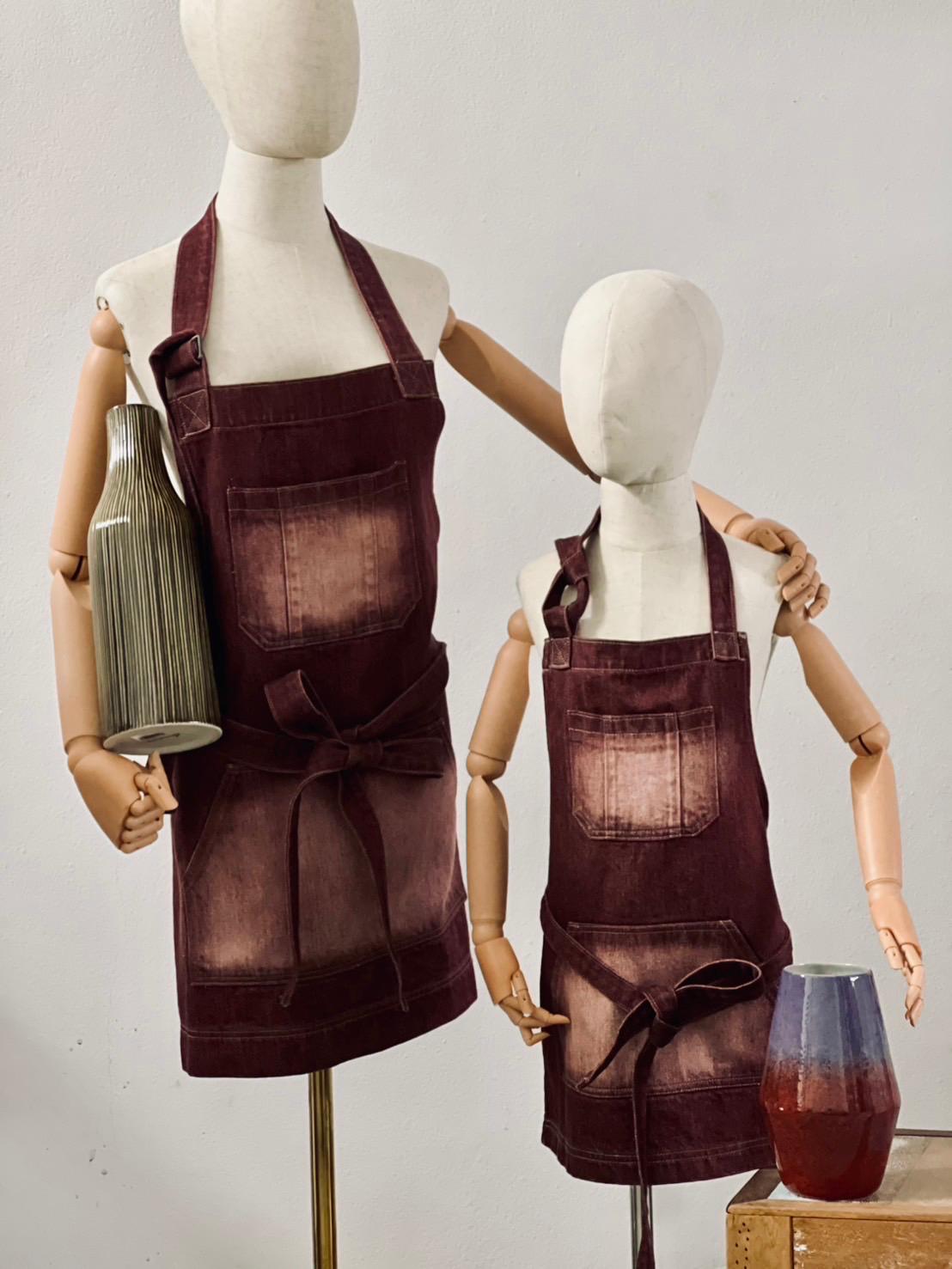 Pottery denim apron in wine shown with a glazed ceramic vase, adult and child set