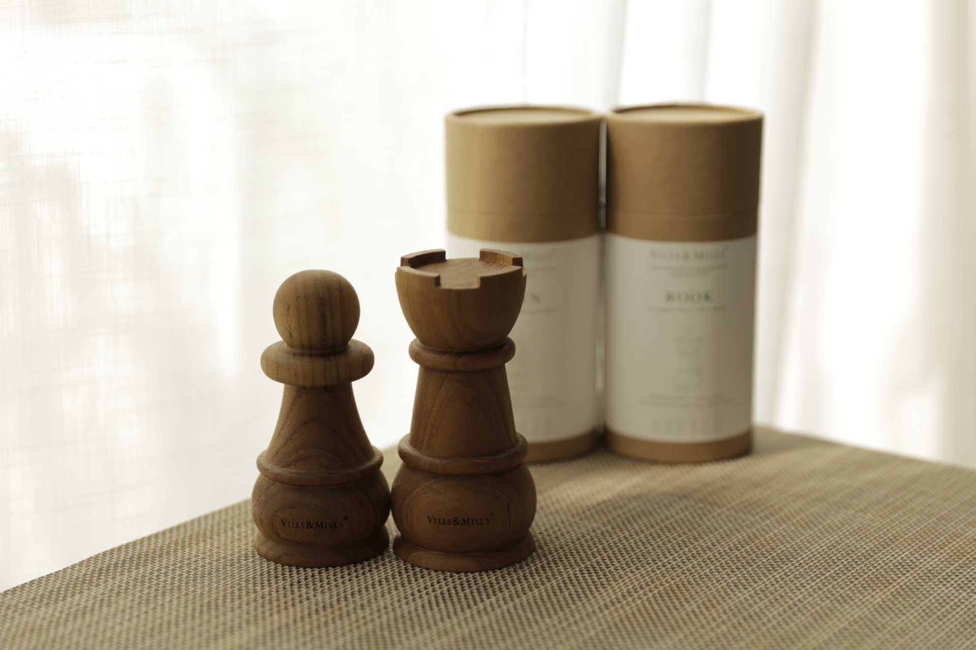 Pawn and Rook salt and pepper mills in solid teak beside their PAWN and ROOK packaging tubes